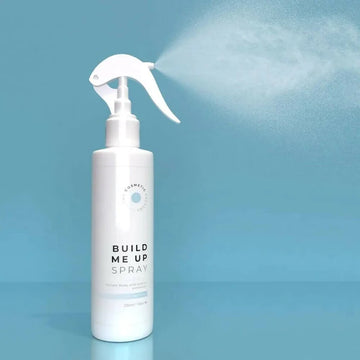 a bottle of build me up spray 225ml against a blue background with mist.